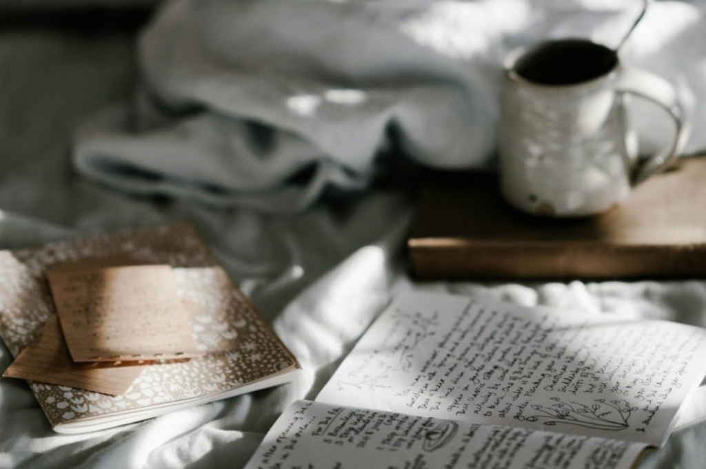 Picture of a bed/sofa with scattered notebooks and a warm drink